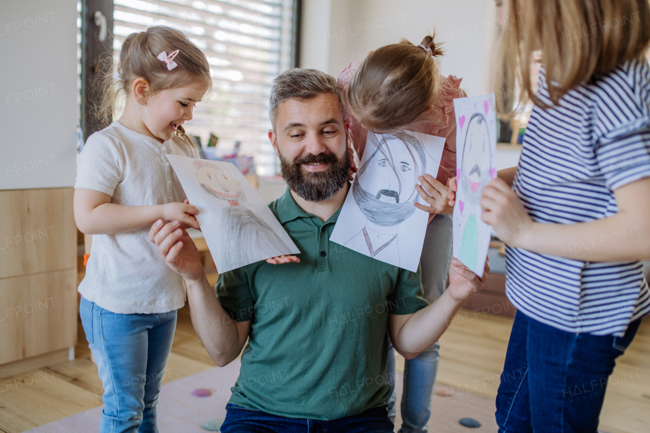 A father of three little daughters getting drawings from them at home.