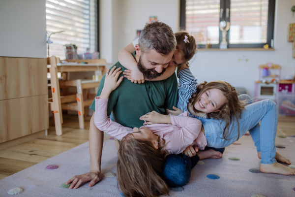 A cheerful father with three little daughters playing together at home.