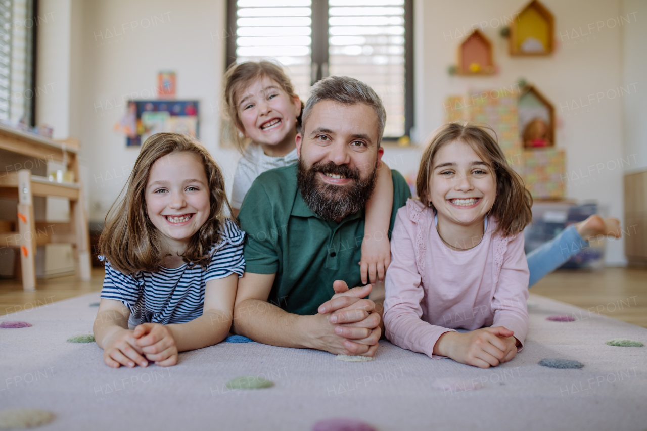 A cheerful father with three little daughters playing together at home.