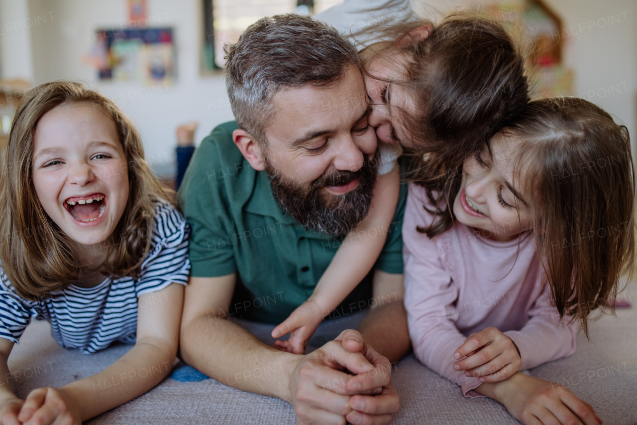 A cheerful father with three little daughters playing together at home.