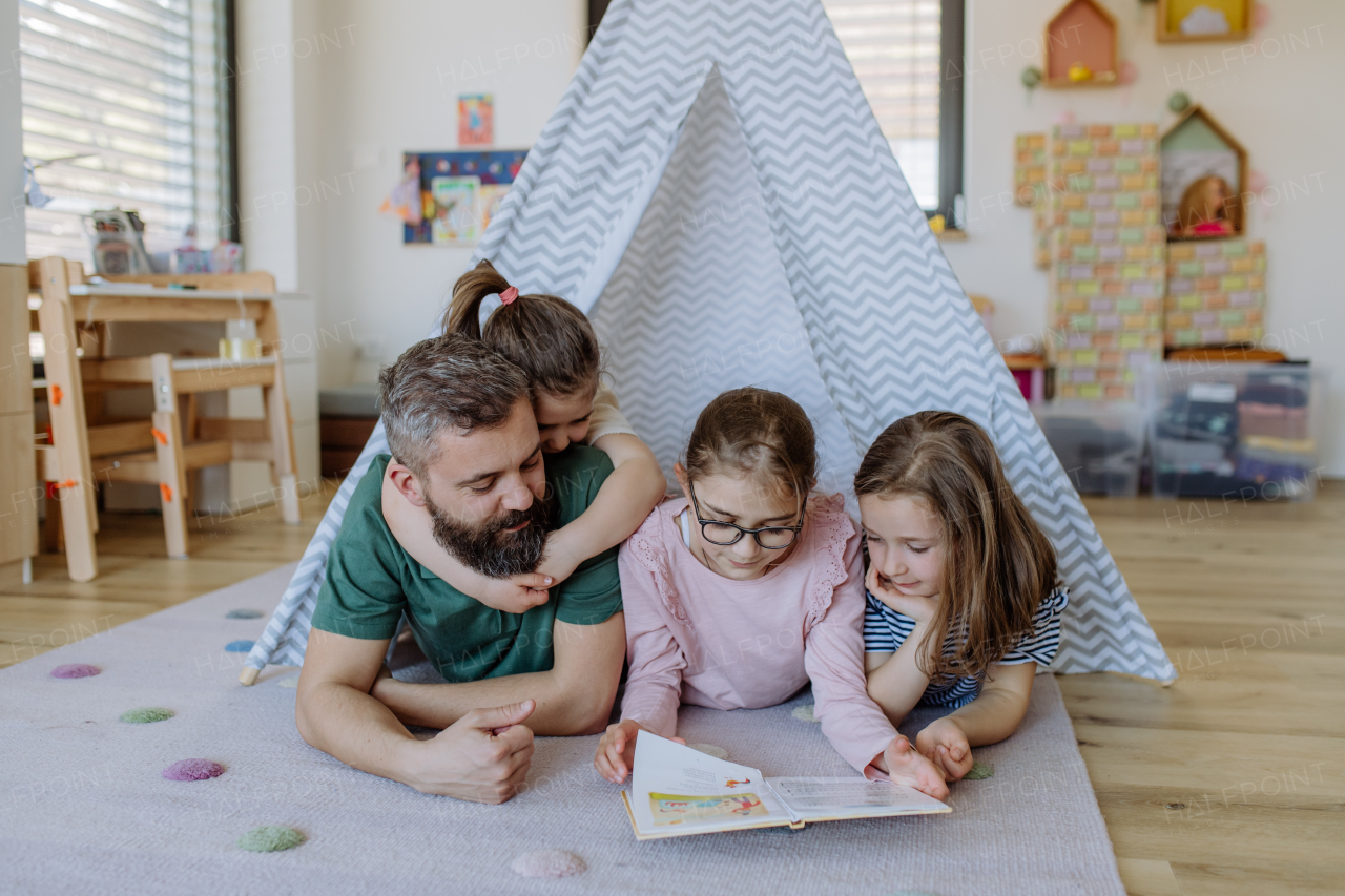 A cheerful father of three little daughters reading them book at home.