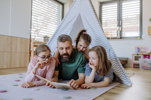 A cheerful father of three little daughters reading them book at home.