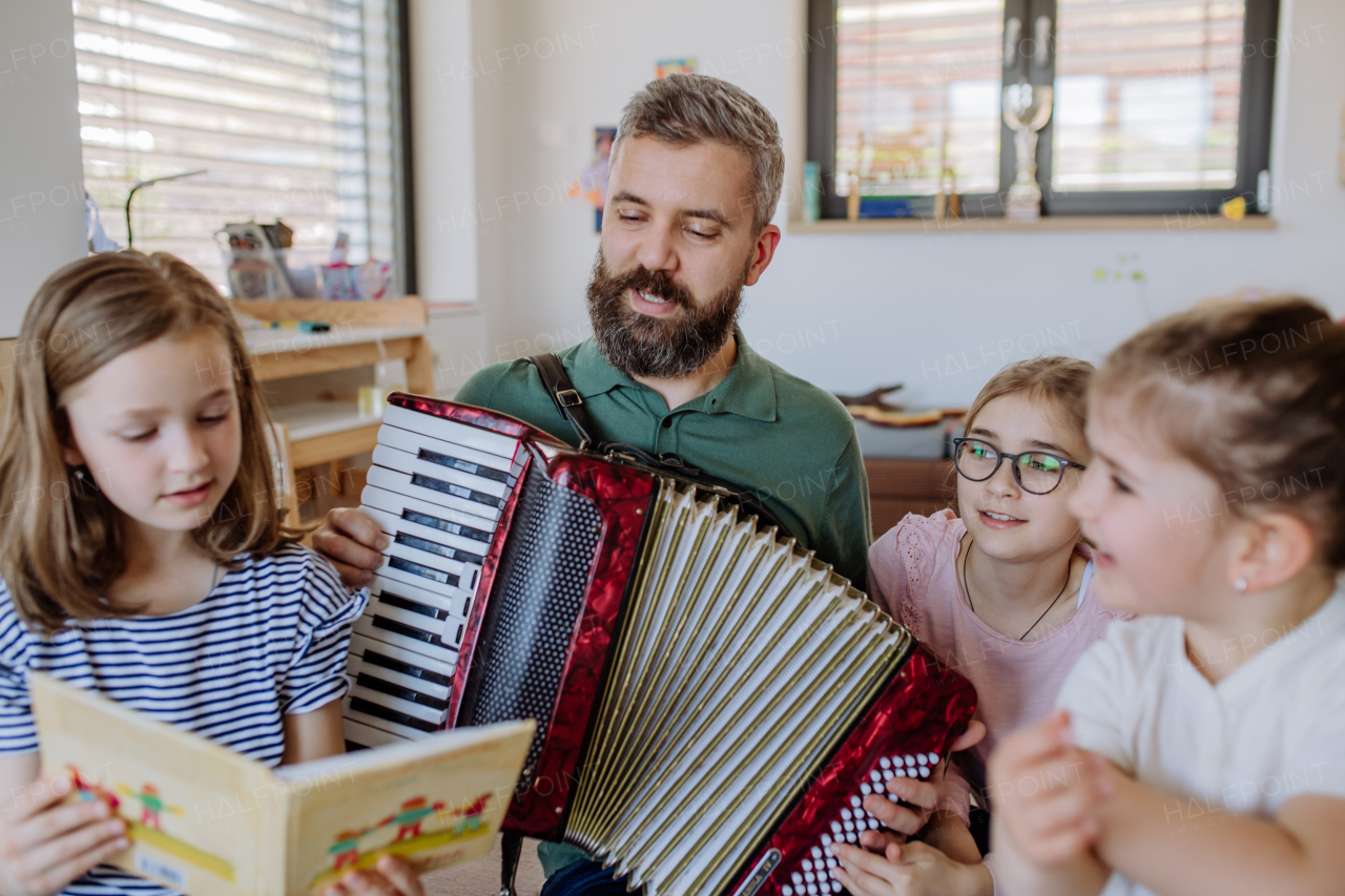 A cheerful father musician playing the accordion to his three little daughters at home.