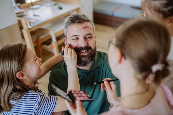 Three little girls putting on make up on their father, a fathers day with daughters at home.