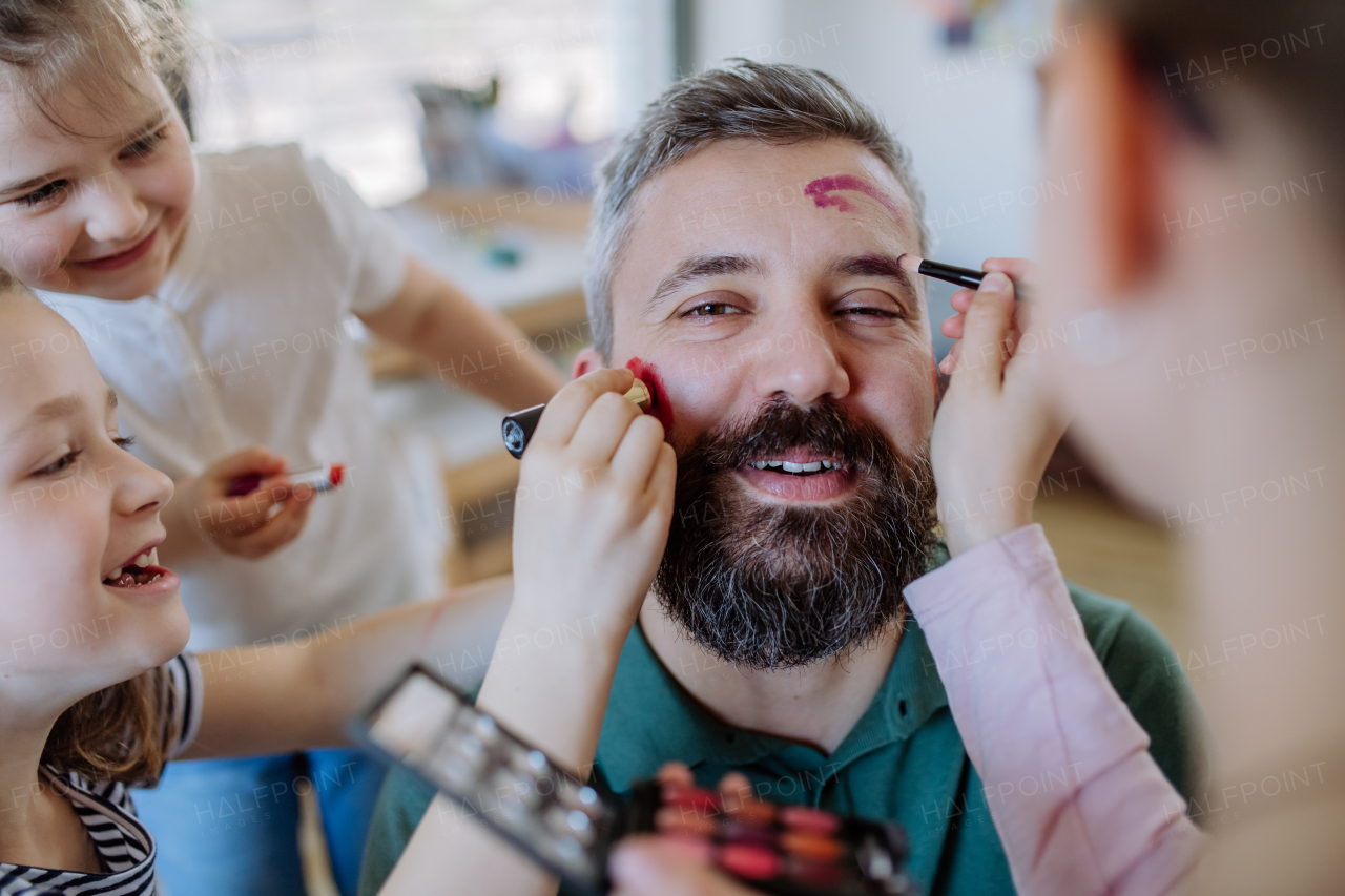 Three little girls putting on make up on their father, a fathers day with daughters at home.