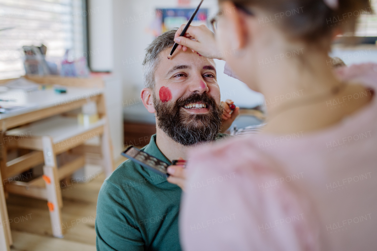 A little daughter putting on make up on her father at home.