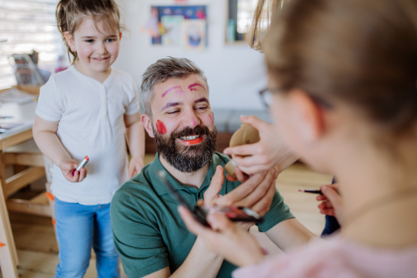 Three little girls putting on make up on their father, a fathers day with daughters at home.