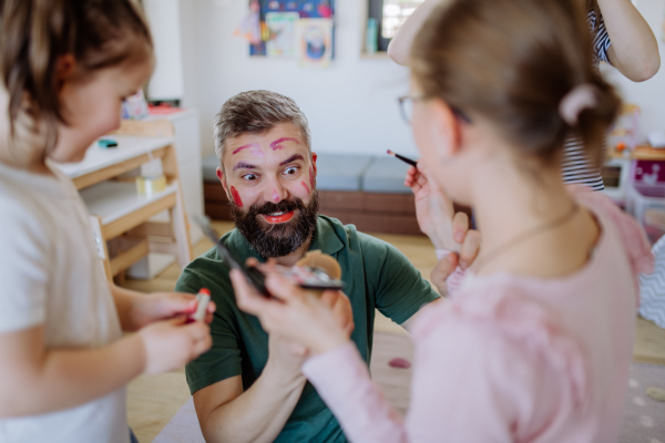 Three little girls putting on make up on their father, a fathers day with daughters at home.