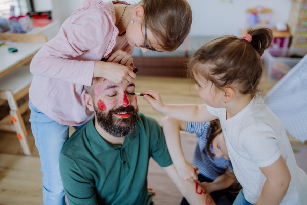 Three little girls putting on make up on their father, a fathers day with daughters at home.