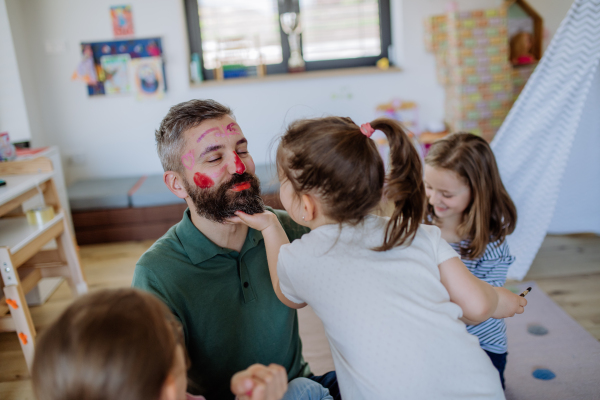 Three little girls putting on make up on their father, a fathers day with daughters at home.