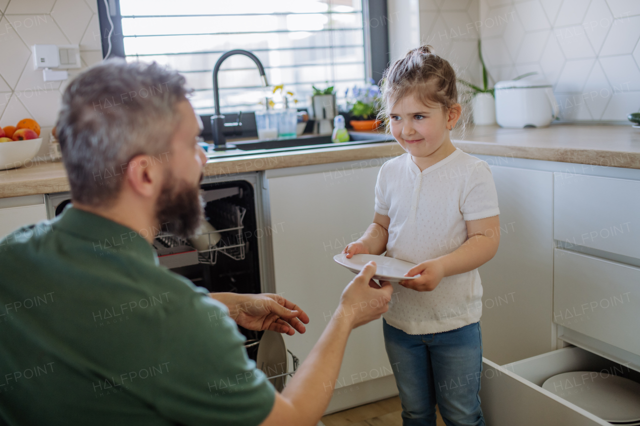 A little girl helping his father to unlad dishwasher in kitchen at home.