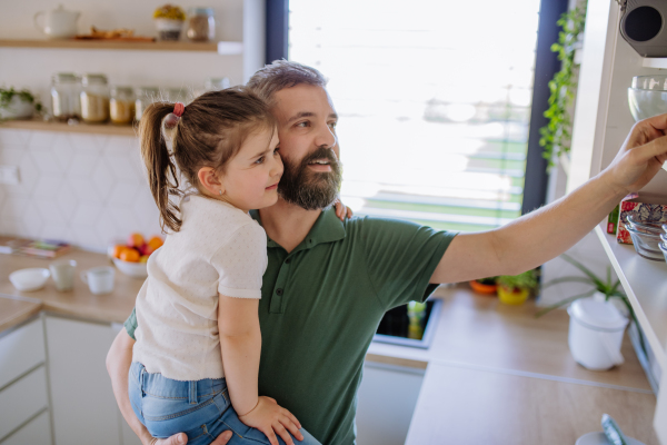 A little girl with her father in kitchen at home, daily chores concept.