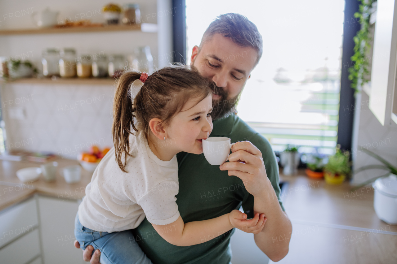 A father giving his little daughter cup with tea to drink at home.