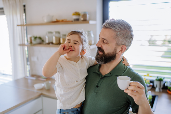 A father giving his little daughter cup with tea to drink at home.