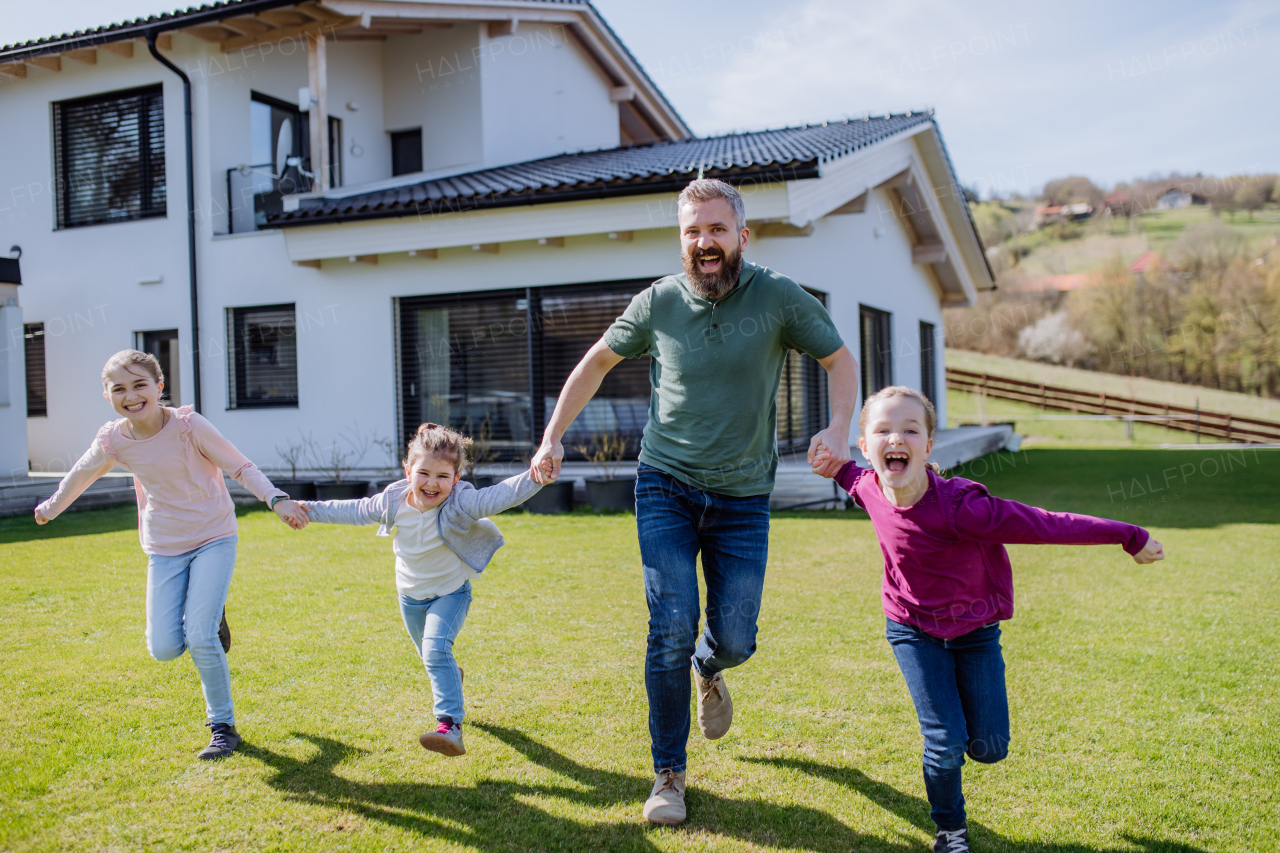 A cheerful ather with his three little daughters holding hands and running in garden.