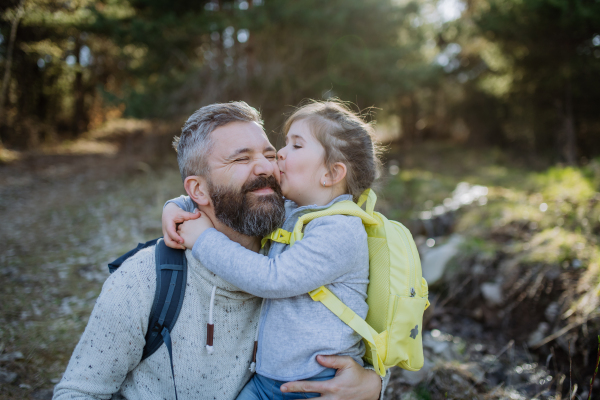 A little daughter kissing her father during walk in spring nature together.