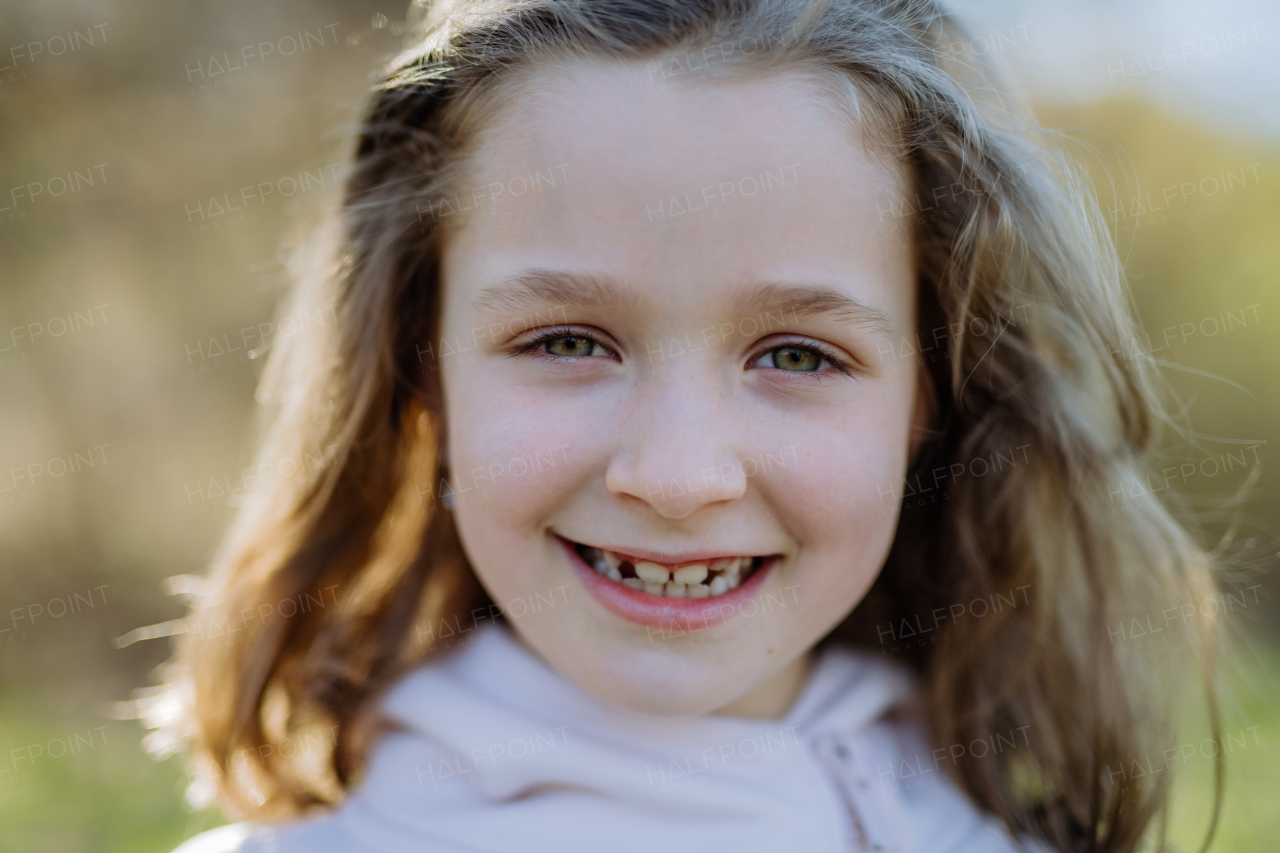 Portrait of pretty child girl standing in summer park looking in camera smiling happily.