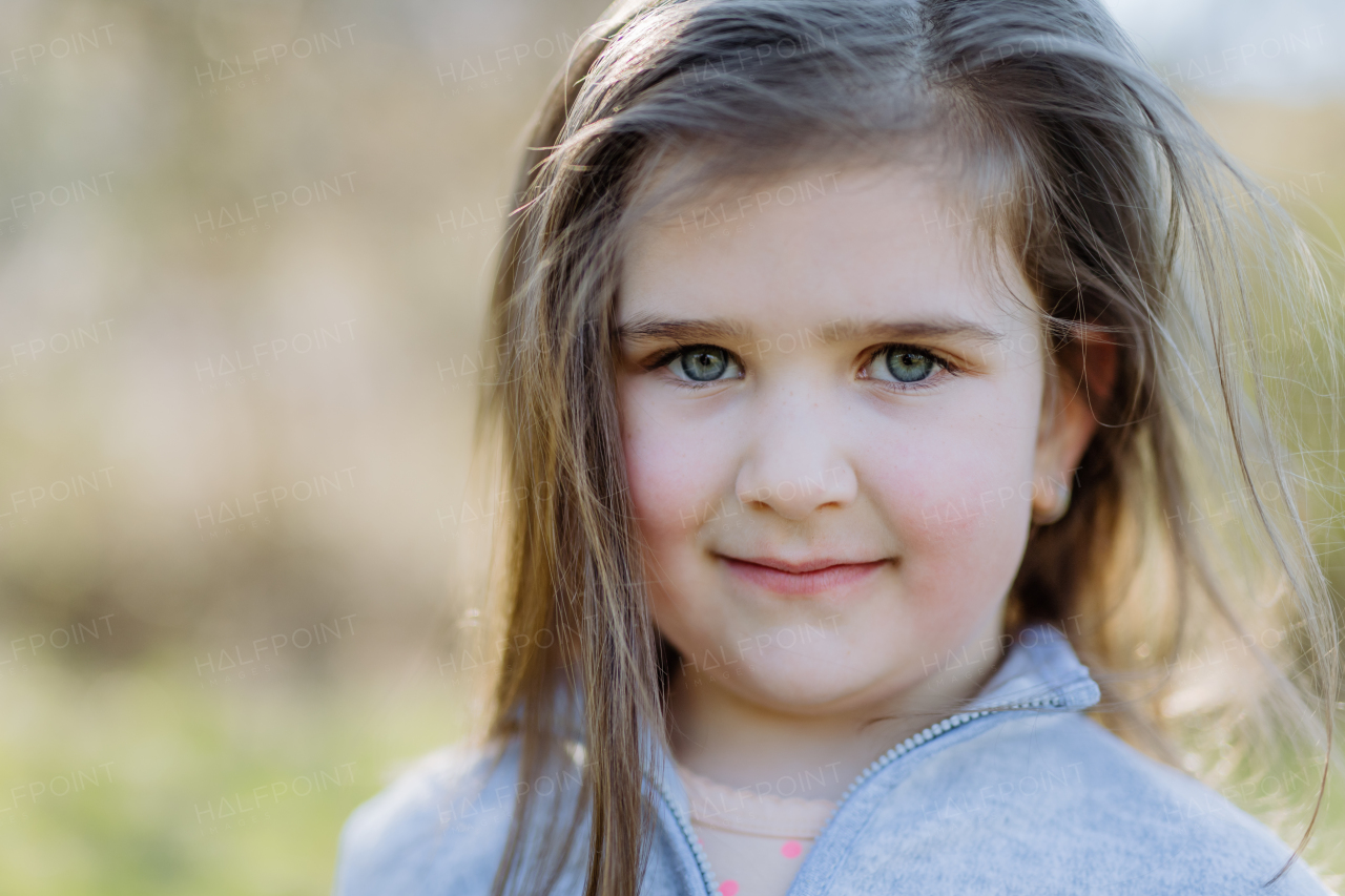 Portrait of pretty child girl standing in summer park looking in camera smiling happily.