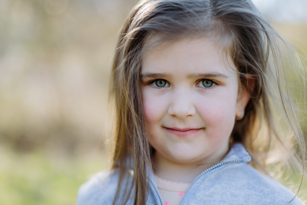 Portrait of pretty child girl standing in summer park looking in camera smiling happily.