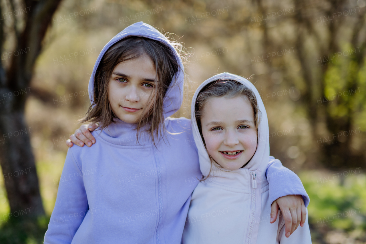 Two little sisters looking at a camera in spring nature together.