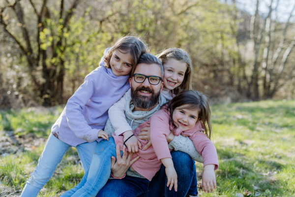 A father with his three little daughters looking at camera in spring nature together.