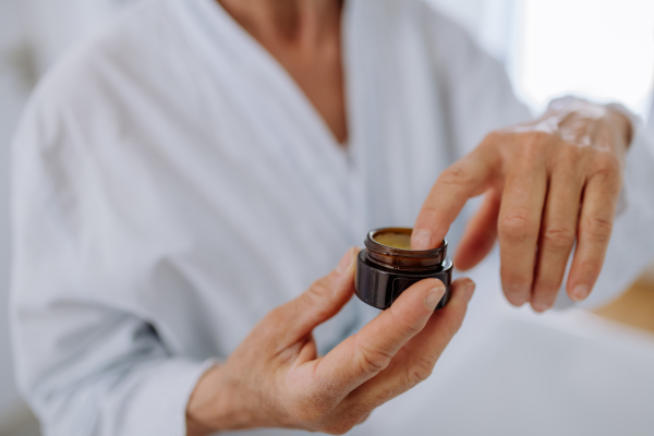 A beautiful senior woman in bathrobe applying natural face cream in bathroom, skin care and morning routine concept.