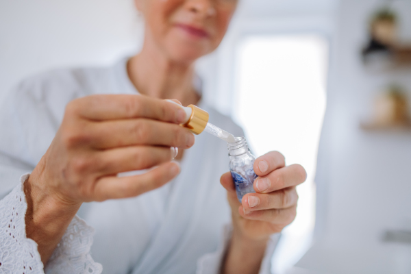 A close-up of senior woman holding skin serum with pipette, natural woman beauty skincare cosmetic product.