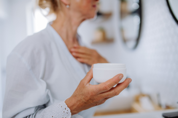 A beautiful senior woman in bathrobe applying natural cream in bathroom, skin care and morning routine concept.