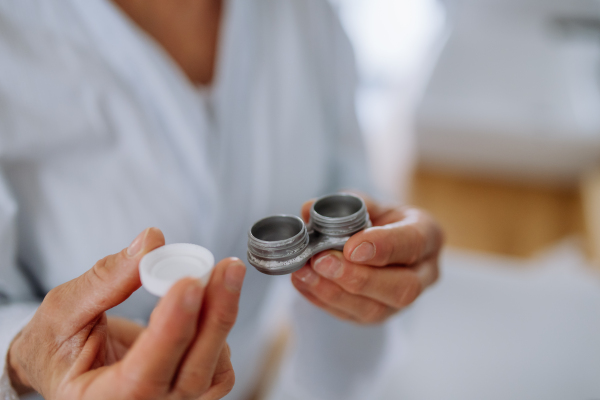 A senior woman holding plastic case with contact lenses in bathroom at home, morning routine concept.