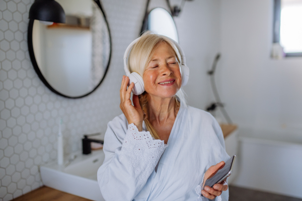 A beautiful senior woman in bathrobe drinking tea in bathroom, relax and wellness concept.