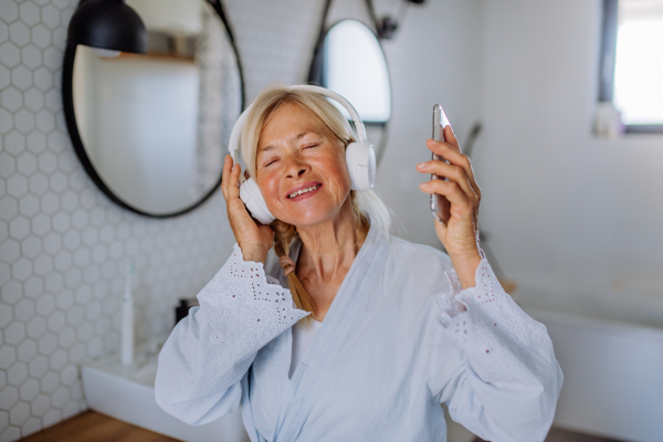 A beautiful senior woman in bathrobe drinking tea in bathroom, relax and wellness concept.