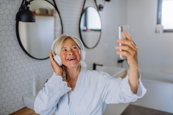 A beautiful senior woman in bathrobe drinking tea in bathroom, relax and wellness concept.