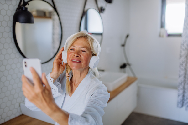 A beautiful senior woman in bathrobe drinking tea in bathroom, relax and wellness concept.