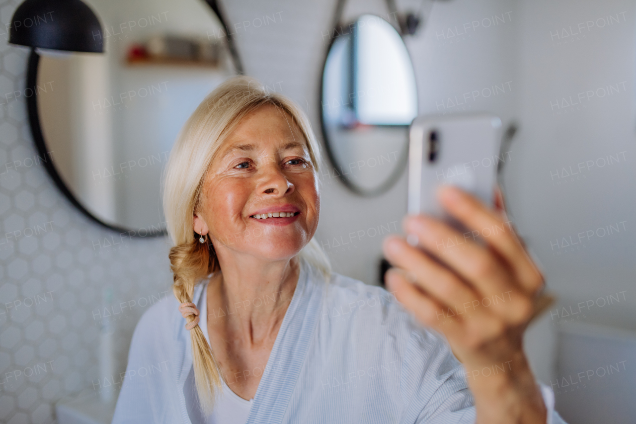 A cheerful senior woman in bathrobe listening to music in bathroom, relax and wellness concept.