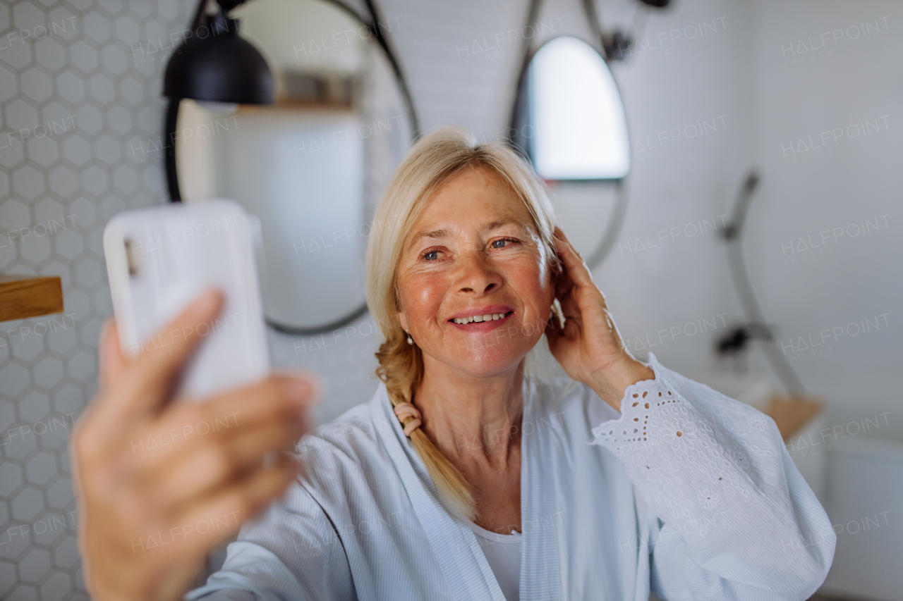 A cheerful senior woman in bathrobe listening to music in bathroom, relax and wellness concept.