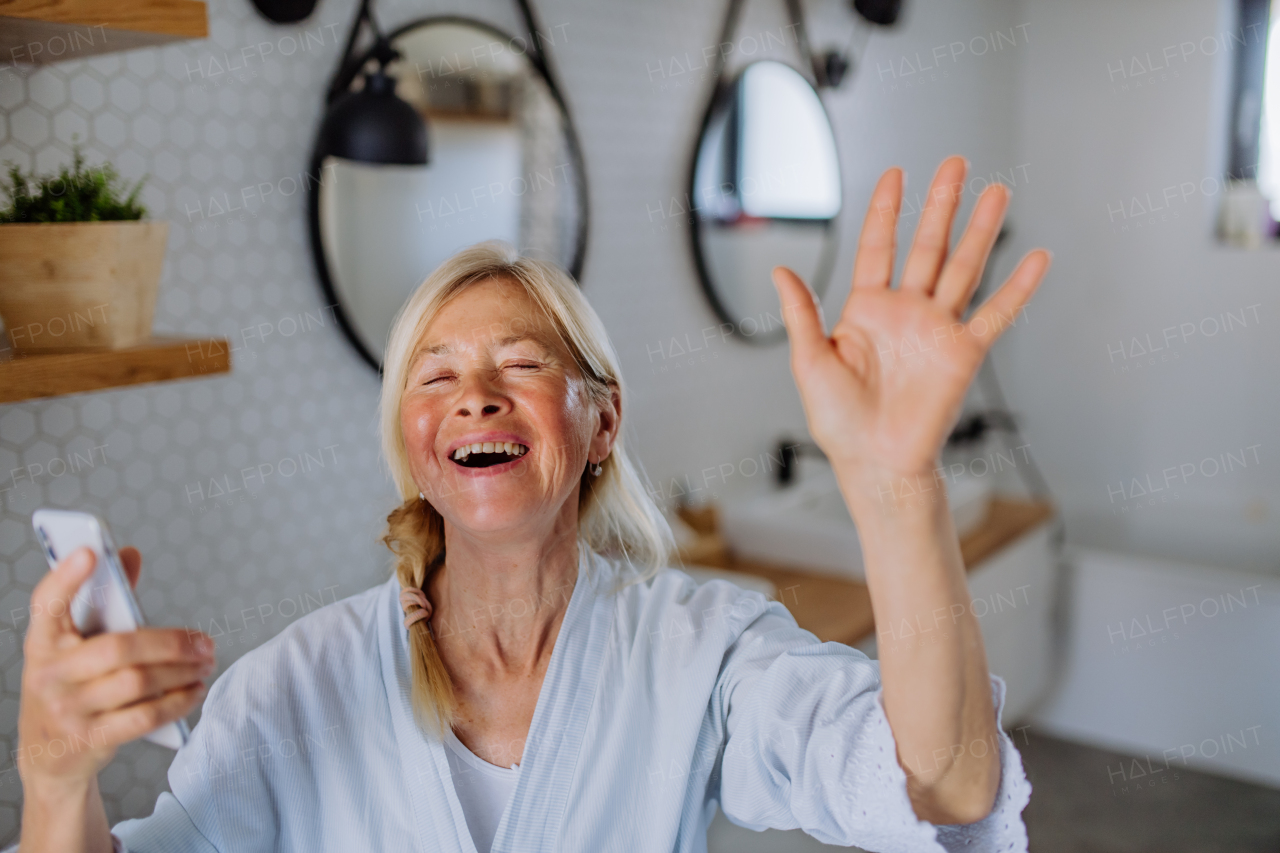 A cheerful senior woman in bathrobe listening to music in bathroom, relax and wellness concept.