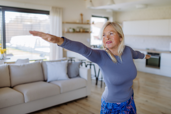 A fit senior woman doing stretching exercise at home, active lifestyle concept.