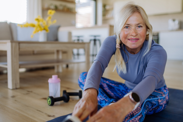 A fit senior woman doing stretching exercise at home, active lifestyle concept.