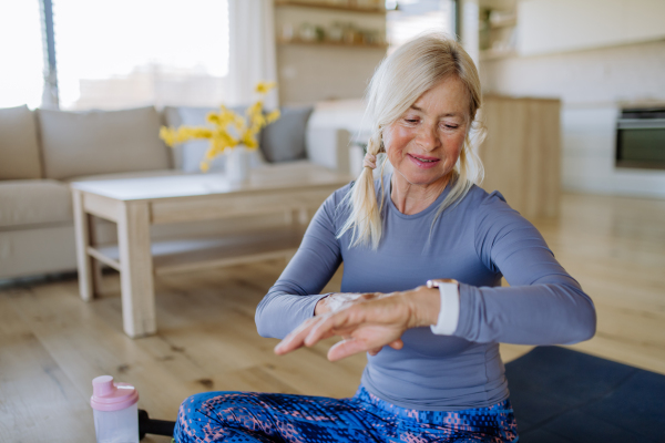 A fit senior woman setting and looking at sports smartwatch and checking her performance at home.