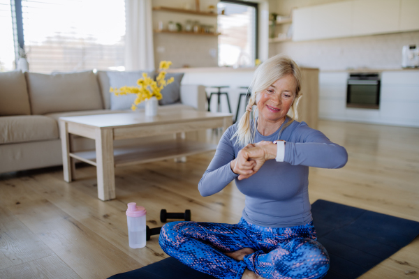 A fit senior woman setting and looking at sports smartwatch and checking her performance at home.