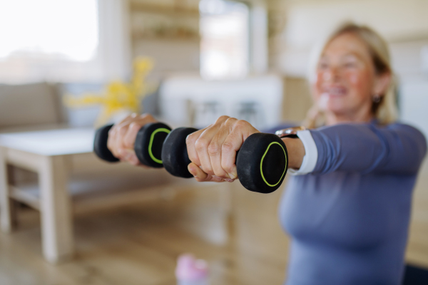 A fit senior woman exercising with dumbbells at home, active lifestyle concept.