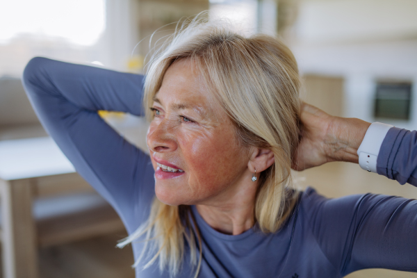 A fit senior woman doing stretching exercise at home, active lifestyle concept.