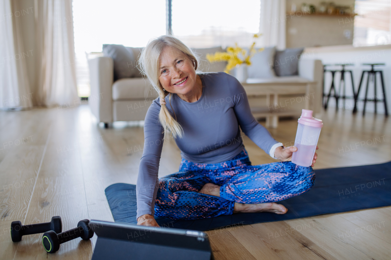 A fit senior woman doing stretching exercise at home with tutorial on tablet, active lifestyle concept.