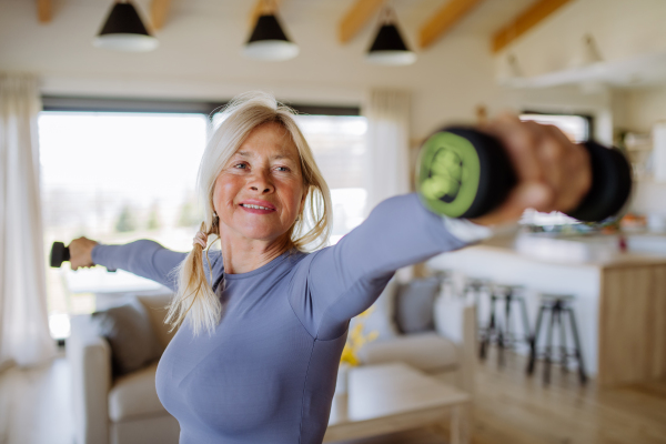 A fit senior woman exercising with dumbbells at home, active lifestyle concept.