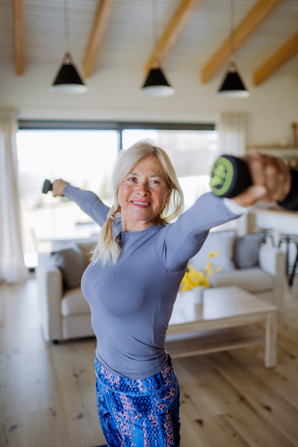 A fit senior woman exercising with dumbbells at home, active lifestyle concept.