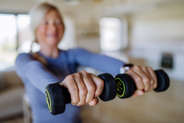 A fit senior woman exercising with dumbbells at home, active lifestyle concept.