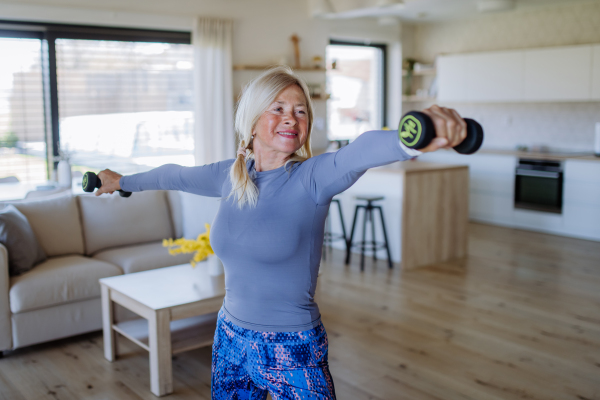 A fit senior woman exercising with dumbbells at home, active lifestyle concept.