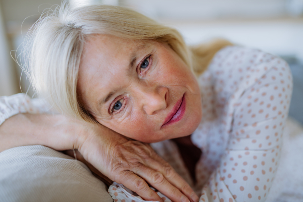 A portrait of sad attractive senior woman sitting on a sofa at home adn contemplating.