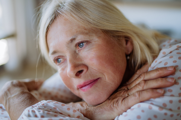 A portrait of sad attractive senior woman sitting on a sofa at home adn contemplating.