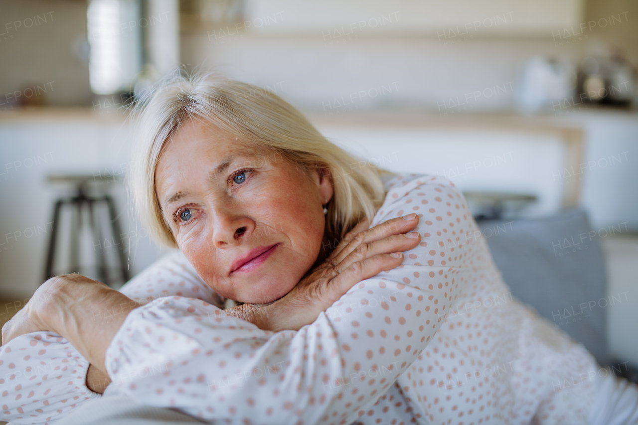 A portrait of sad attractive senior woman sitting on a sofa at home adn contemplating.